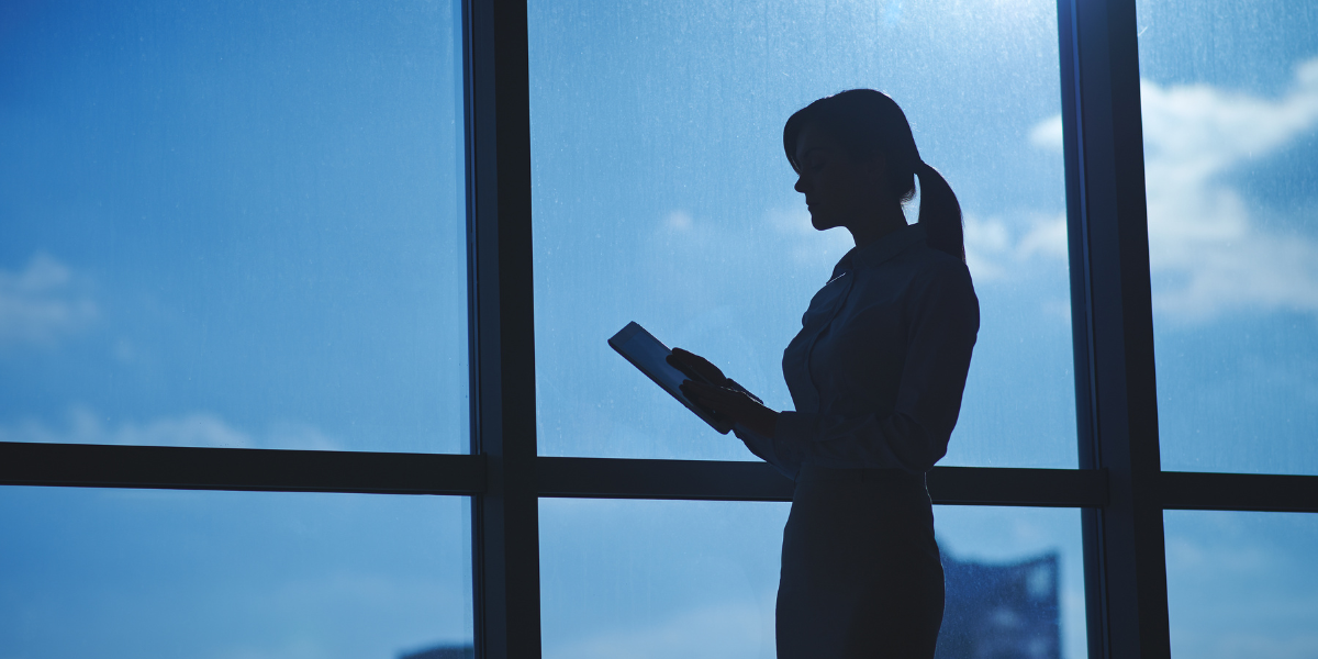 A dark silhouette of a women standing in front of a large window. 