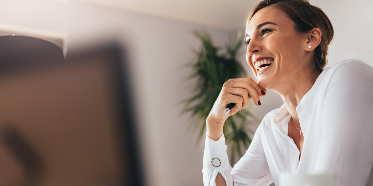 A female business professional, visibly happy thanks to a positive workplace culture, looks at colleagues out of view laughingly. 