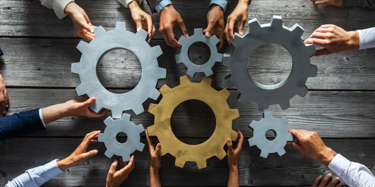 Employees joining gold and silver gears representing how an entire organization must share responsibility for a high-performing corporate culture.