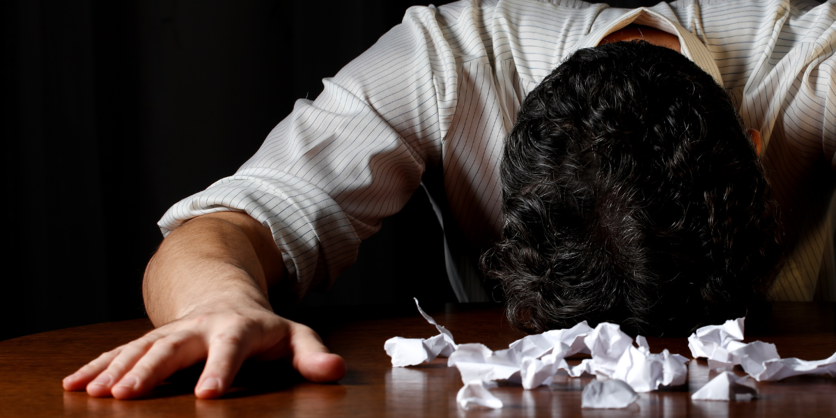 Frustrated businessman with his head on a desk. A torn and crumpled job description document is in front of him.
